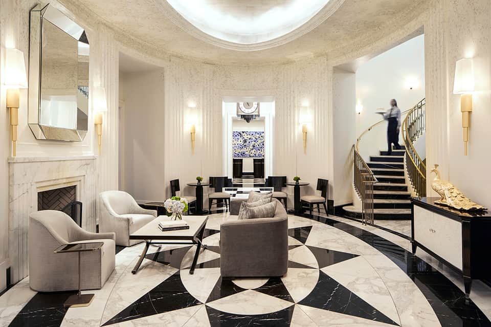 Elegant marble lobby with fireplace, patterned floor, grand staircase, and modern furnishings