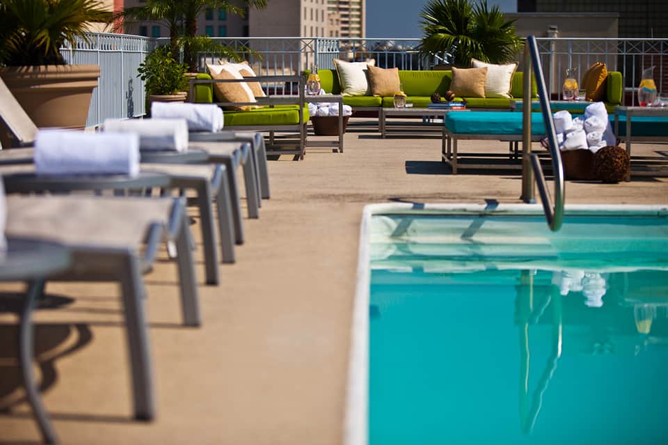 Rooftop pool deck with lime green lounge seating, turquoise pool, towel service, and city skyline views