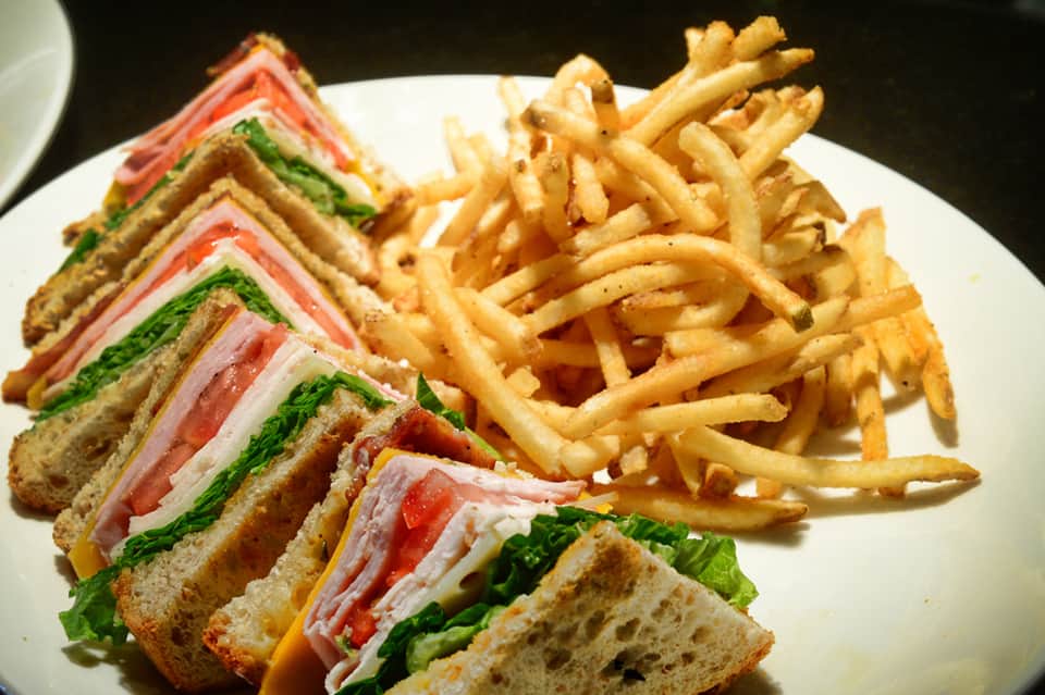 Club sandwich with ham, lettuce, tomato, and crispy french fries on white plate