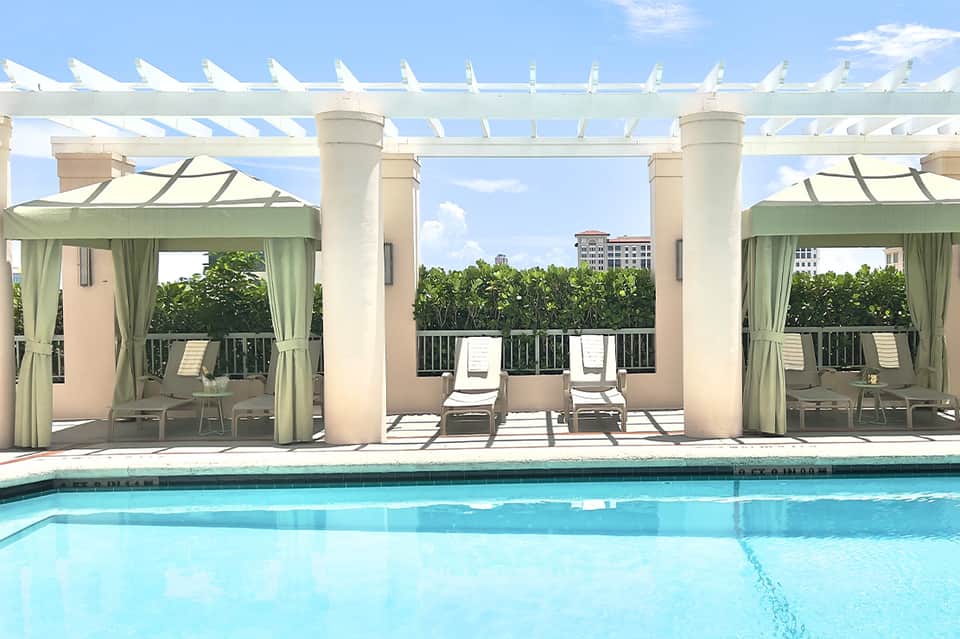 Luxury poolside cabanas with white pergolas, lounge chairs, and ocean view backdrop