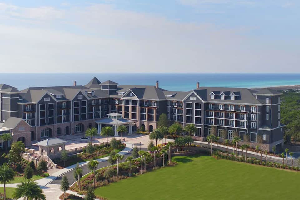 Beachfront resort buildings overlooking ocean with landscaped grounds and palm trees