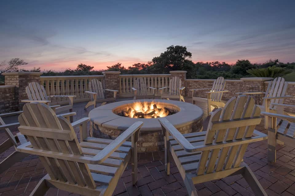 Rooftop fire pit surrounded by Adirondack chairs at dusk with stone walls and trees