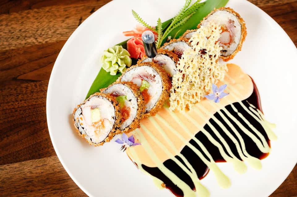 Artfully plated sushi roll with decorative sauce design on white plate