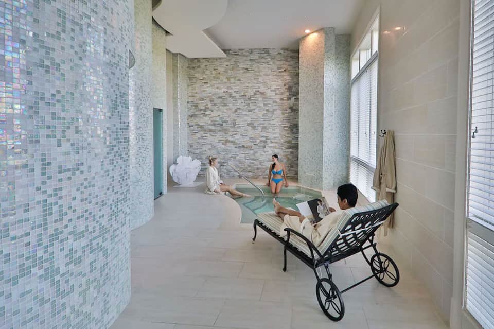 Modern spa area with mosaic tile walls, hot tub, and guests relaxing indoors
