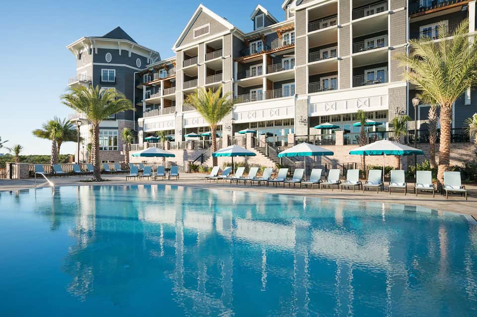 Resort pool with turquoise water, lounge chairs, umbrellas, and multi-story accommodations