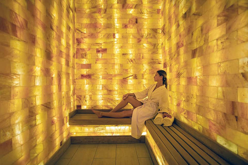 Woman in spa robe relaxing in golden salt therapy room with illuminated walls