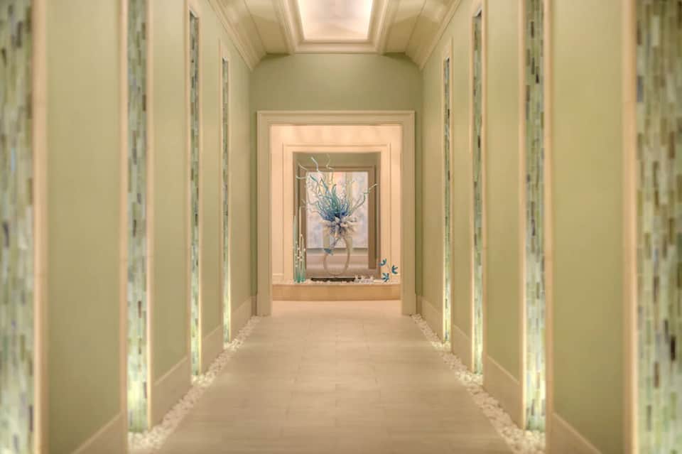 Elegant hallway with cream walls, recessed lighting, and blue floral arrangement in window niche