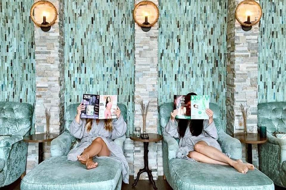 Spa relaxation lounge with turquoise velvet recliners, reading materials, and brass sconces