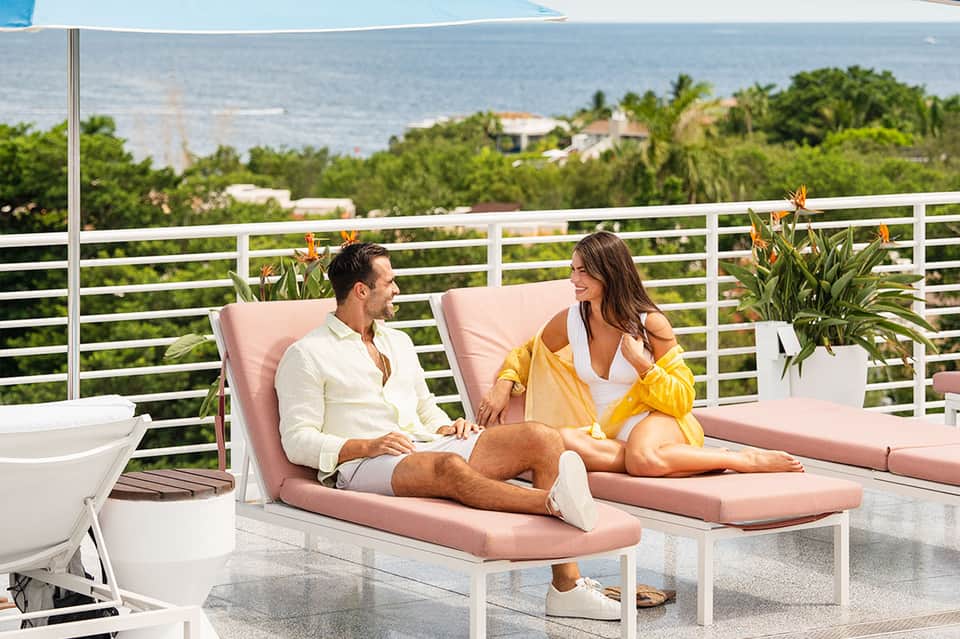 Couple relaxing on pink lounge chairs on terrace overlooking ocean and tropical vegetation