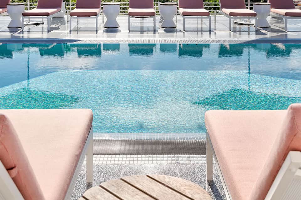 Modern pool deck with pink lounge chairs, turquoise water, and white seating area