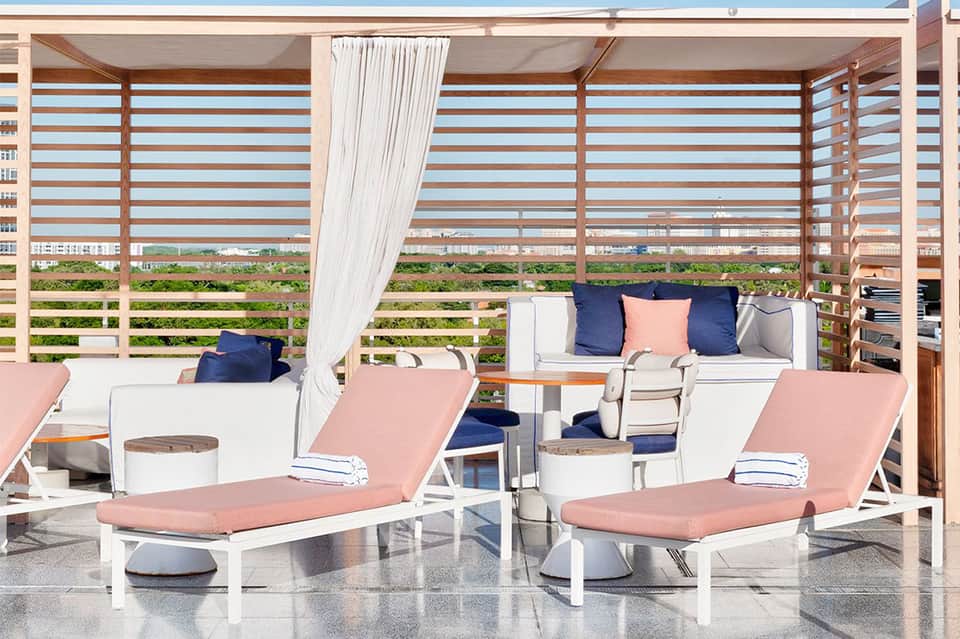 Modern poolside lounge chairs with pink cushions under striped shade structure