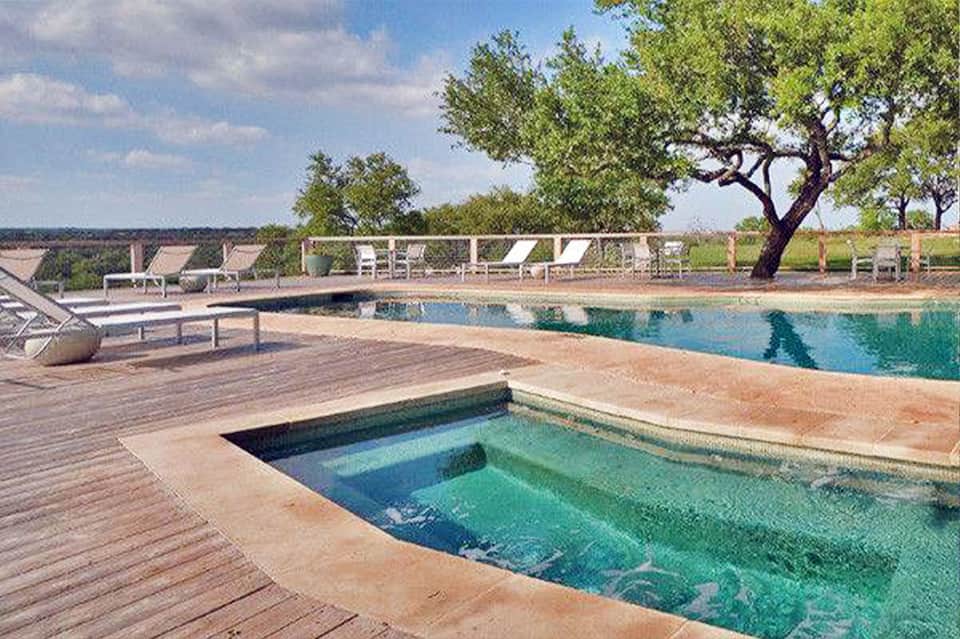 Resort pool with wooden deck, lounge chairs, and scenic countryside view with trees