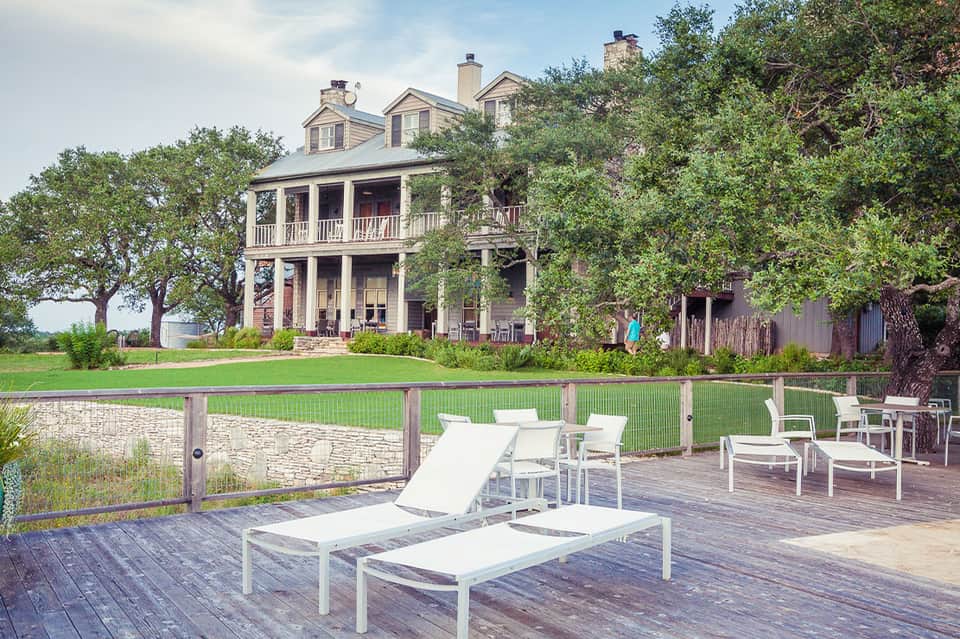 Historic farmhouse with white loungers on wooden deck overlooking manicured lawn