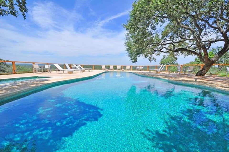 Crystal-clear rectangular swimming pool with loungers and large tree, rural hillside view