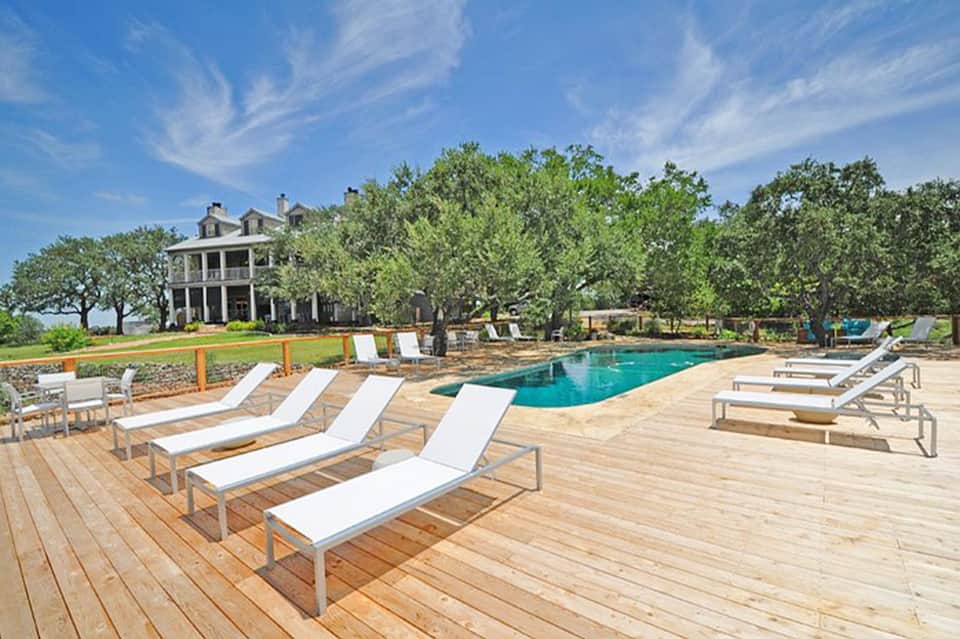 Resort pool deck with lounge chairs, vintage plantation house, and mature shade trees