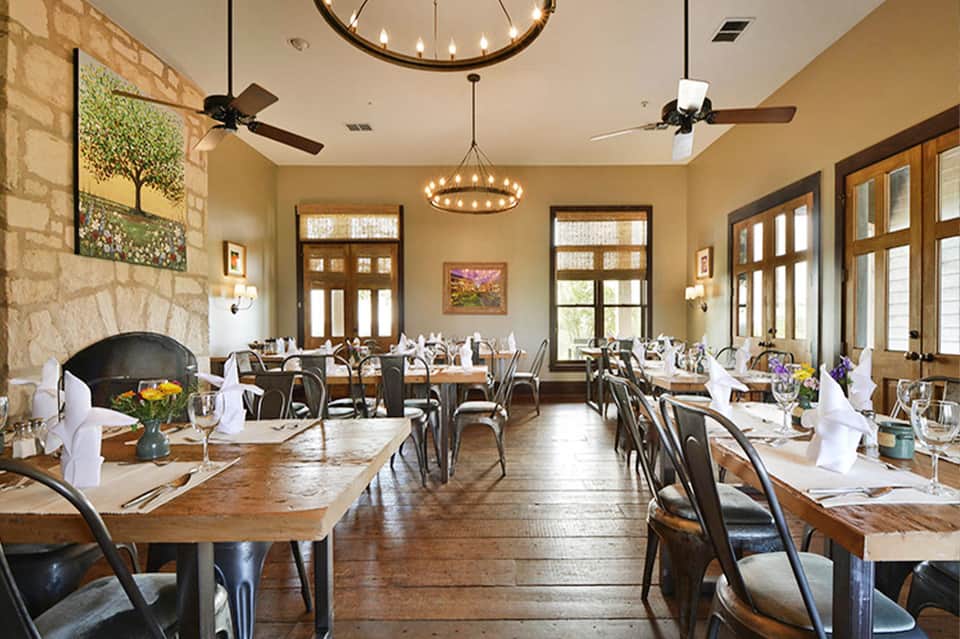 Fine dining restaurant with stone fireplace, wooden beams, and set tables with white napkins