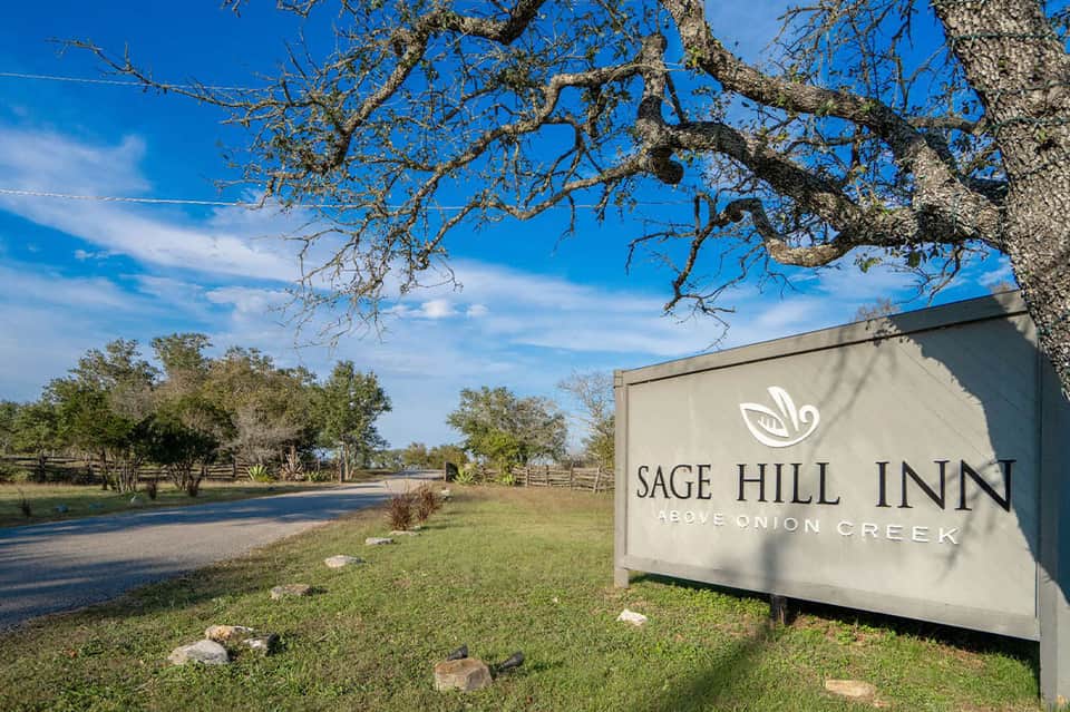 Sage Hill Inn entrance sign on rural grounds with trees and creek landscape