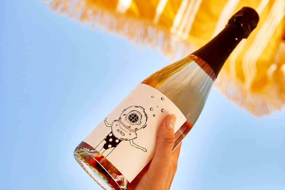 Rosé wine bottle held up against sunny sky with striped beach umbrella in background