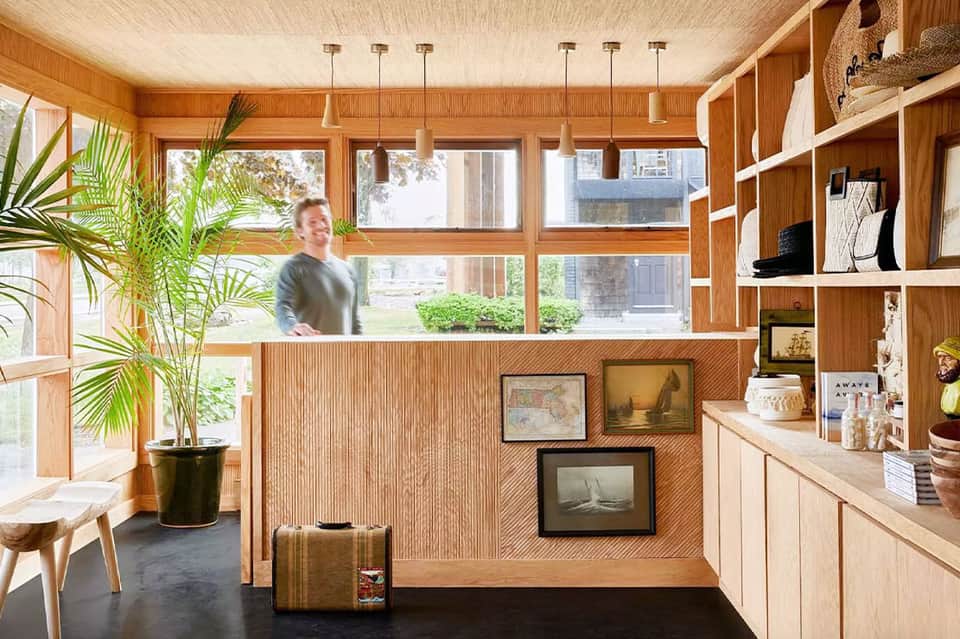 Wooden reception desk with large windows, natural light, modern pendant lights, and decorative shelving