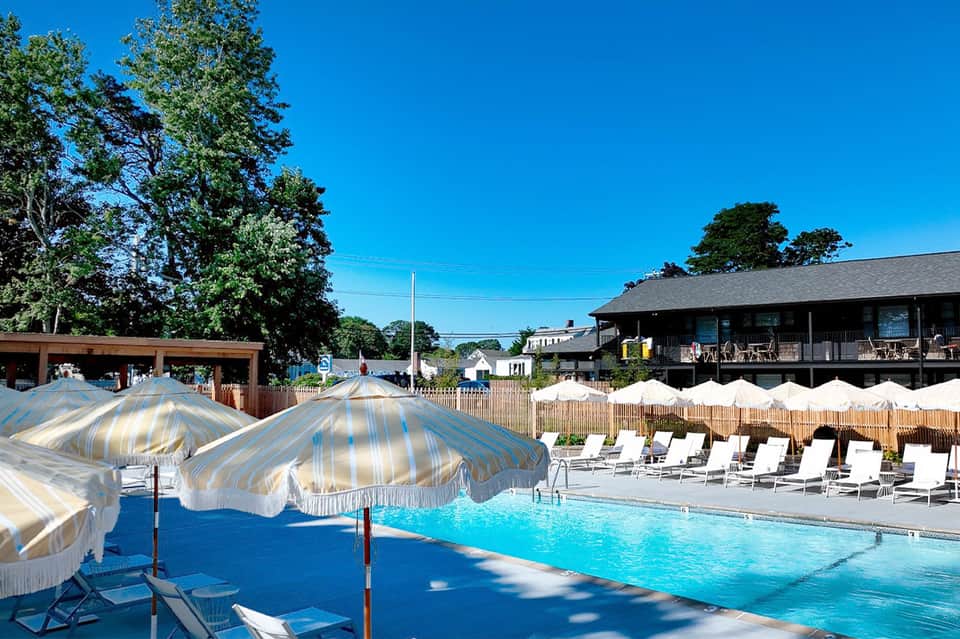 Outdoor pool with striped umbrellas, loungers, wooden structures, and clear blue sky at resort