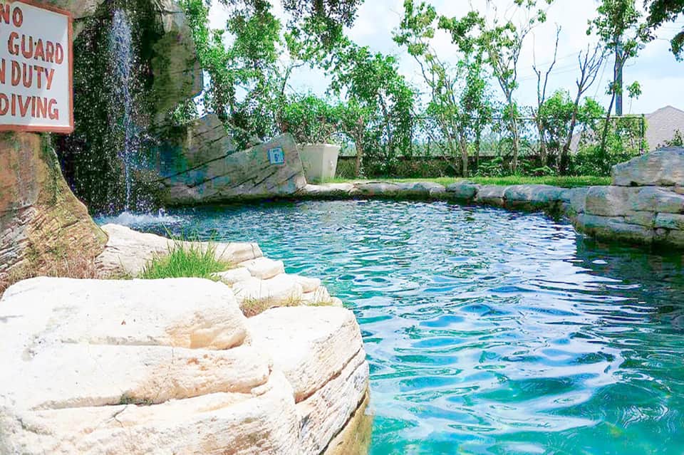 Natural spring-fed pool with turquoise water surrounded by limestone rocks and trees