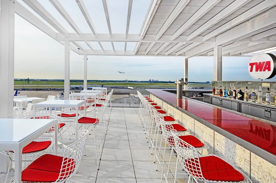 Rooftop dining terrace with red-seated chairs and aircraft runway views