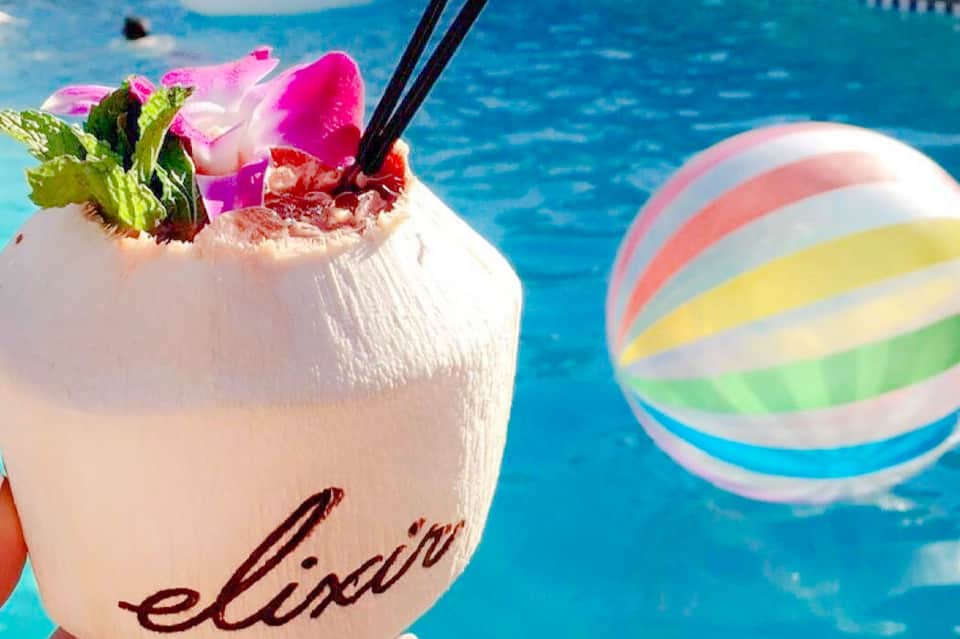 Tropical cocktail with pink flower garnish by pool with colorful beach ball