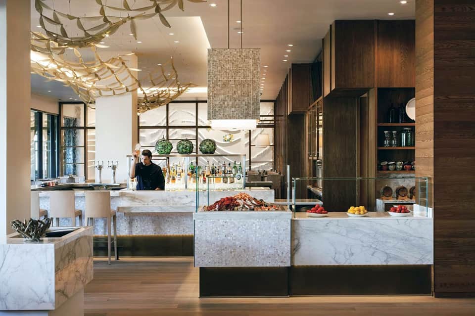 Modern resort bar with marble counters, wood cabinetry, and elegant suspended lighting