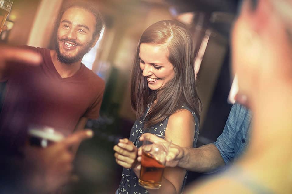 Young adults socializing indoors with drinks in casual, warm-lit setting