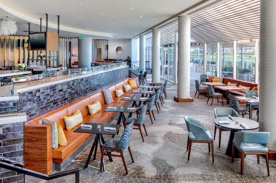 Upscale lounge with orange leather banquette seating, modern bar, and floor-to-ceiling windows