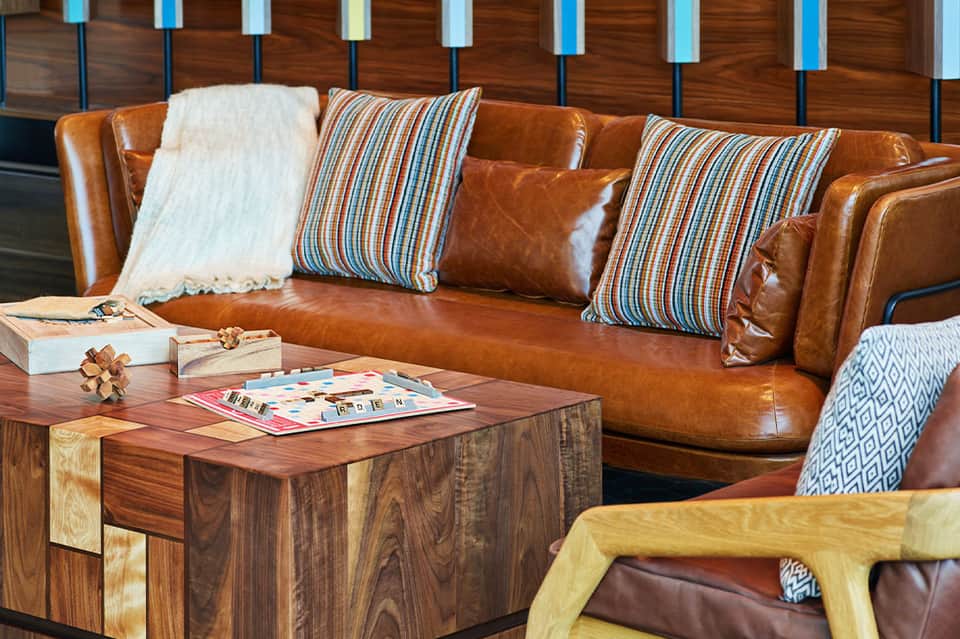 Contemporary hotel lounge with cognac leather sofa, striped pillows, and wooden coffee table