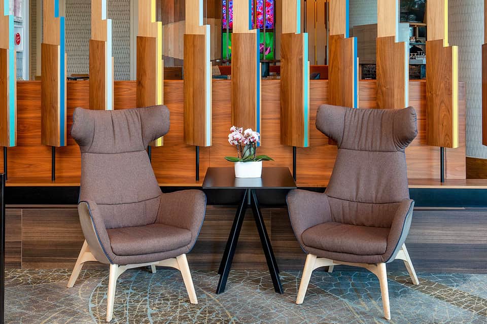 Modern hotel lounge with two gray upholstered chairs separated by small table and decorative wall