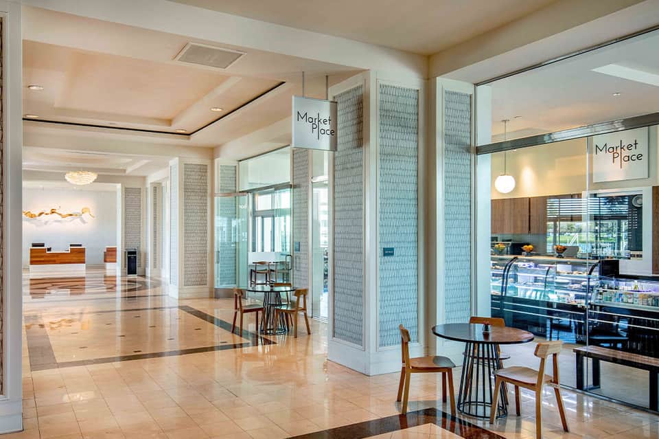 Upscale hotel lobby with polished floors, modern lounge seating, and marketplace dining area with glass partitions