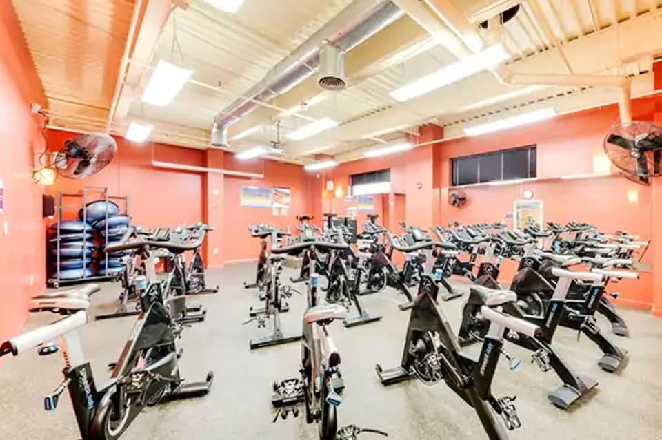 Bright orange fitness studio with rows of stationary spin bikes and exercise equipment