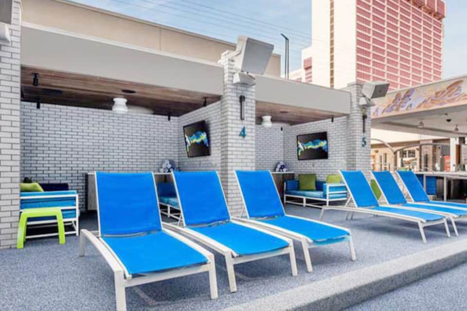 Rooftop pool deck with blue lounge chairs, white umbrellas, and city skyline views