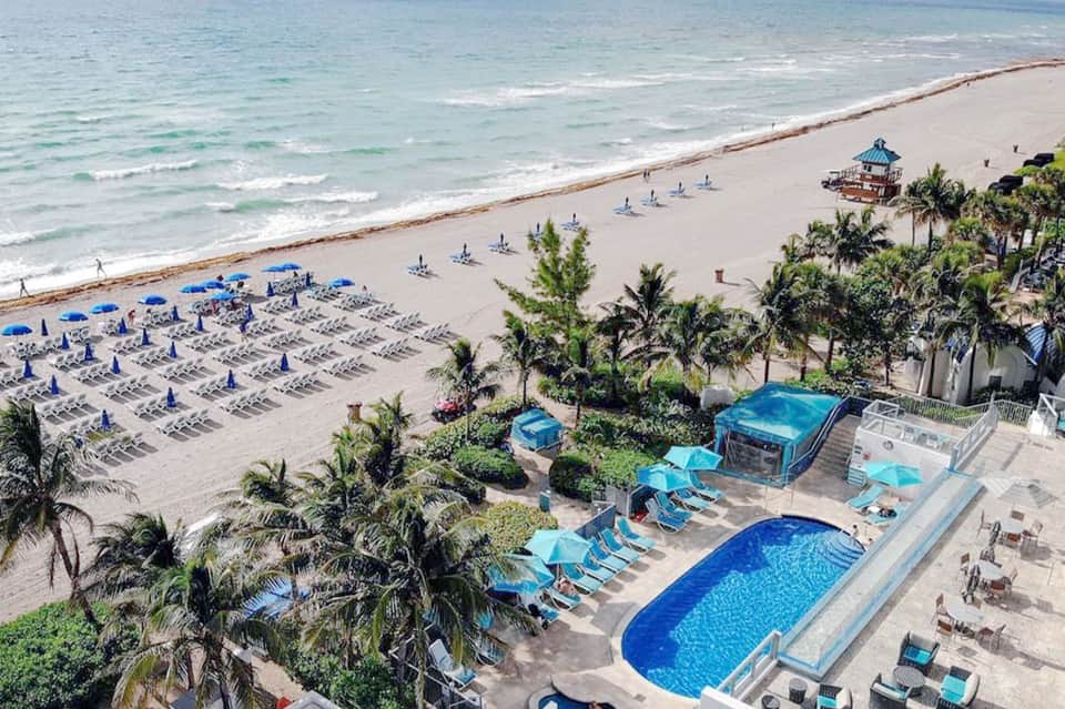 Beach resort aerial view with blue umbrellas, loungers, pools, and ocean coastline