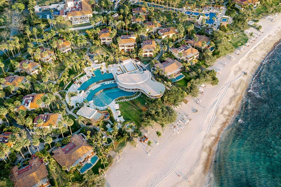 Aerial view of luxury beachfront resort with curved pool, palm-lined grounds, and pristine sandy beach
