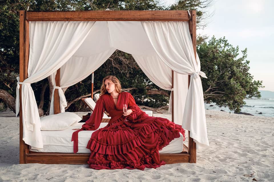 Woman in red dress relaxing in white draped cabana bed on beach near ocean
