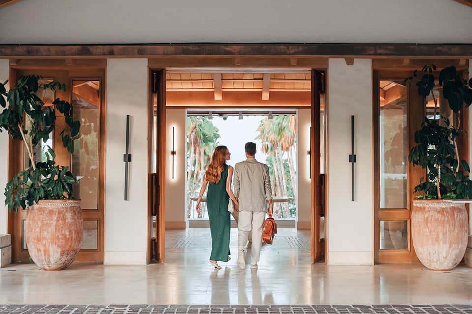 Couple walking through modern hotel lobby with wooden beams and palm tree views