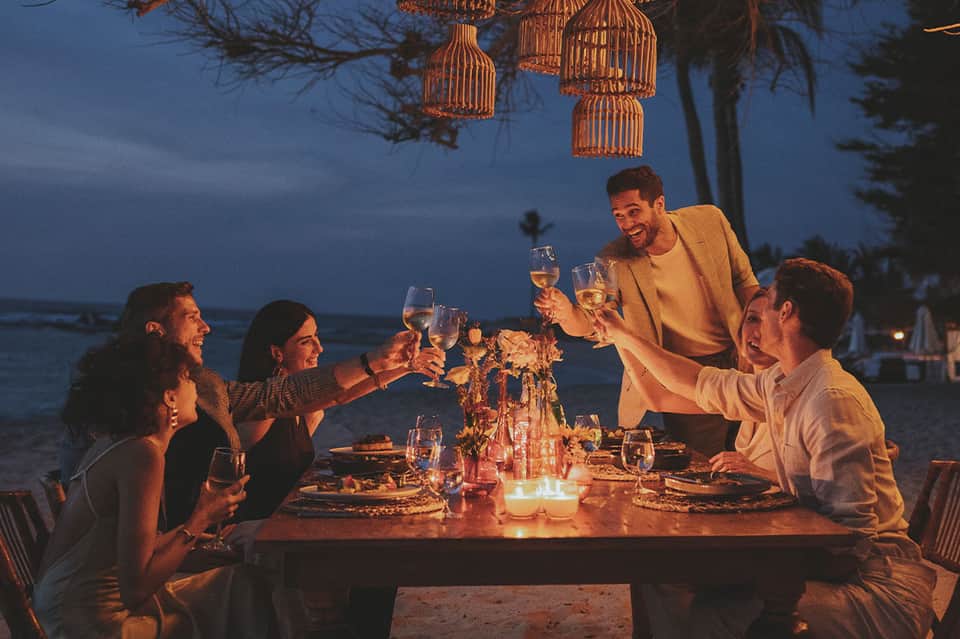 Friends toasting with wine glasses at beachfront dinner table at dusk