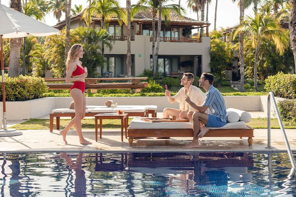 Resort poolside with guests relaxing, palm trees, and modern villa backdrop