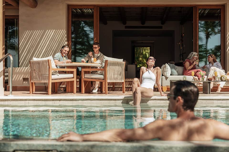 Resort poolside lounge area with guests relaxing on wooden deck and furniture