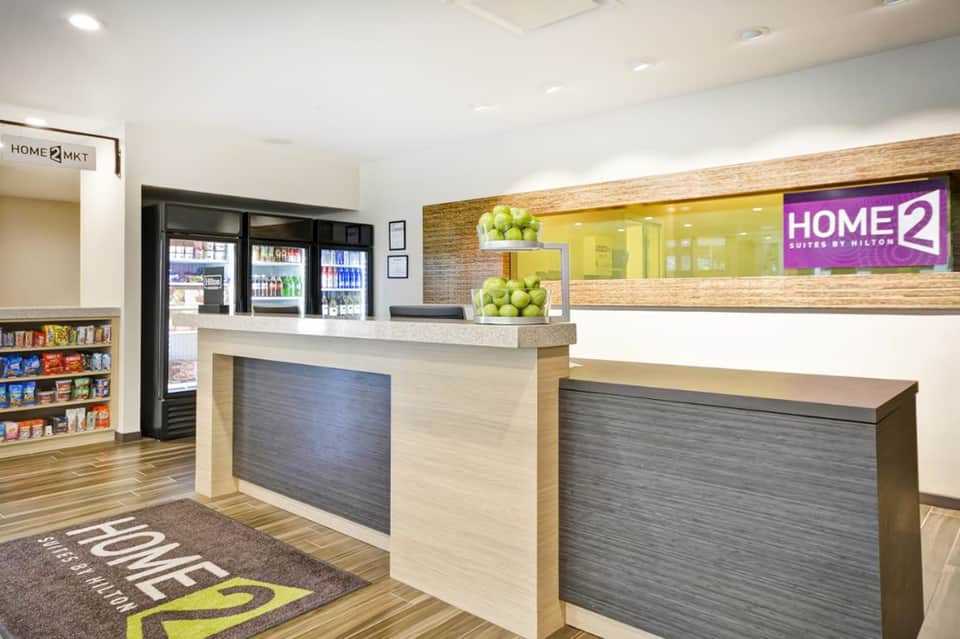 Hotel reception desk with Home2 Suites signage, beverages, and welcoming entry area