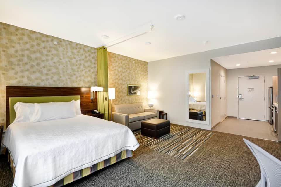 Spacious hotel suite with king bed, sitting area, patterned wallpaper, and modern furnishings