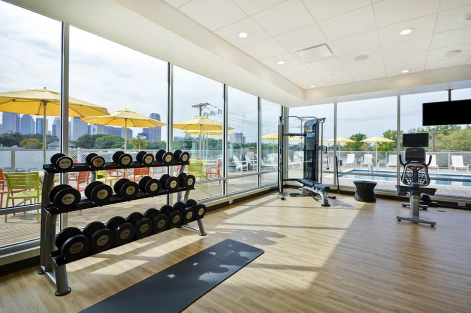 Modern fitness center with dumbbells, cardio equipment, and pool views through windows