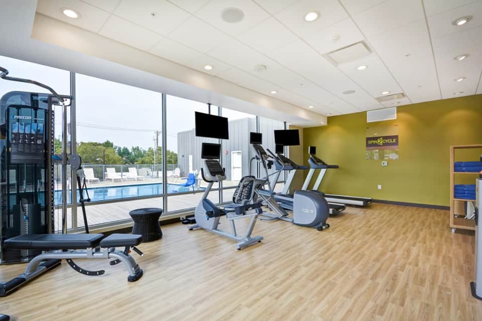 Modern fitness center with exercise equipment, large windows overlooking pool, and yellow accent wall