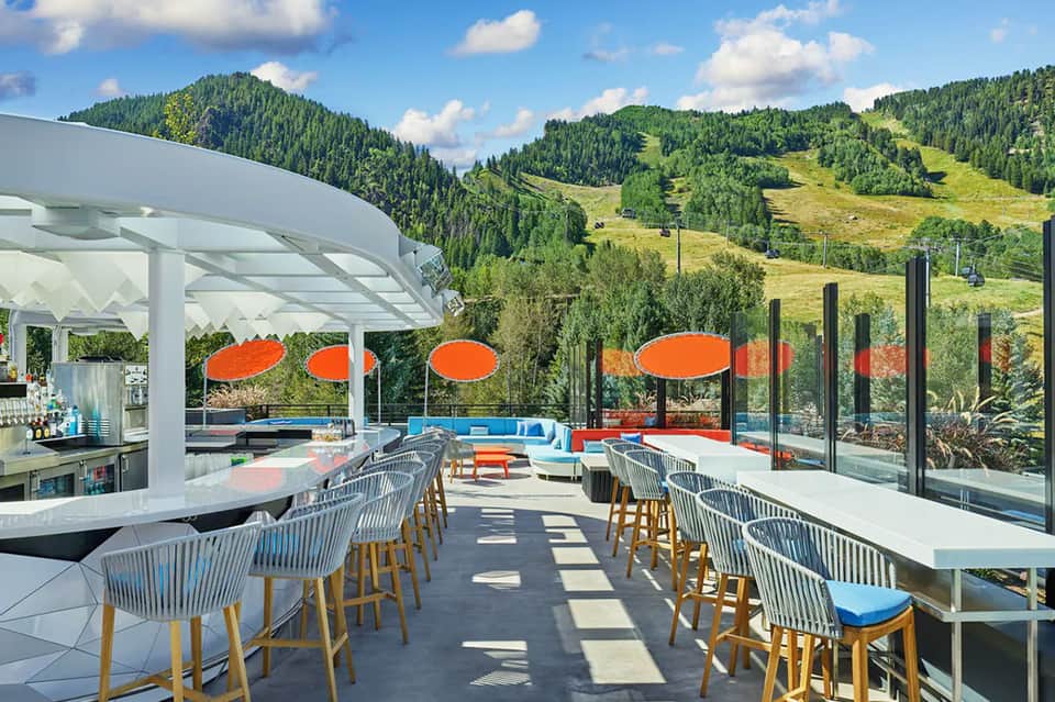 Modern resort deck with bar, orange umbrellas, blue seating, mountain views