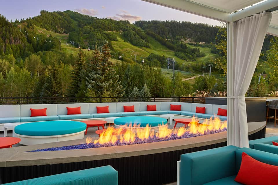 Mountain resort lounge with turquoise curved seating, red pillows, fire pit, and scenic valley views