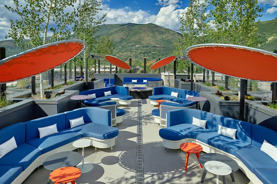 Mountain-view lounge deck with blue modular seating, red umbrellas, white pillows, and scenic valley backdrop