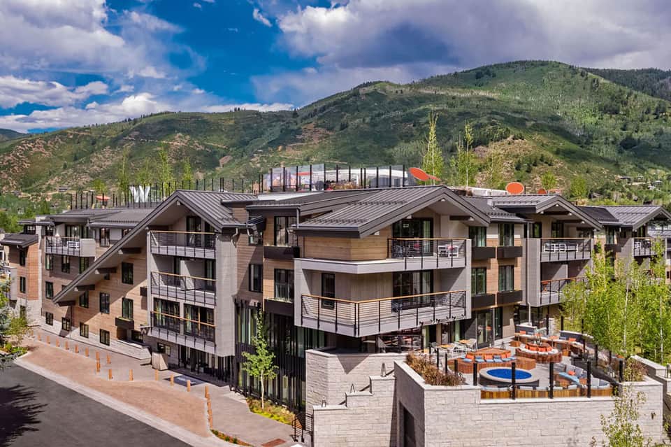 Modern mountain resort building with multiple balconies, rooftop terrace, and forested hillside